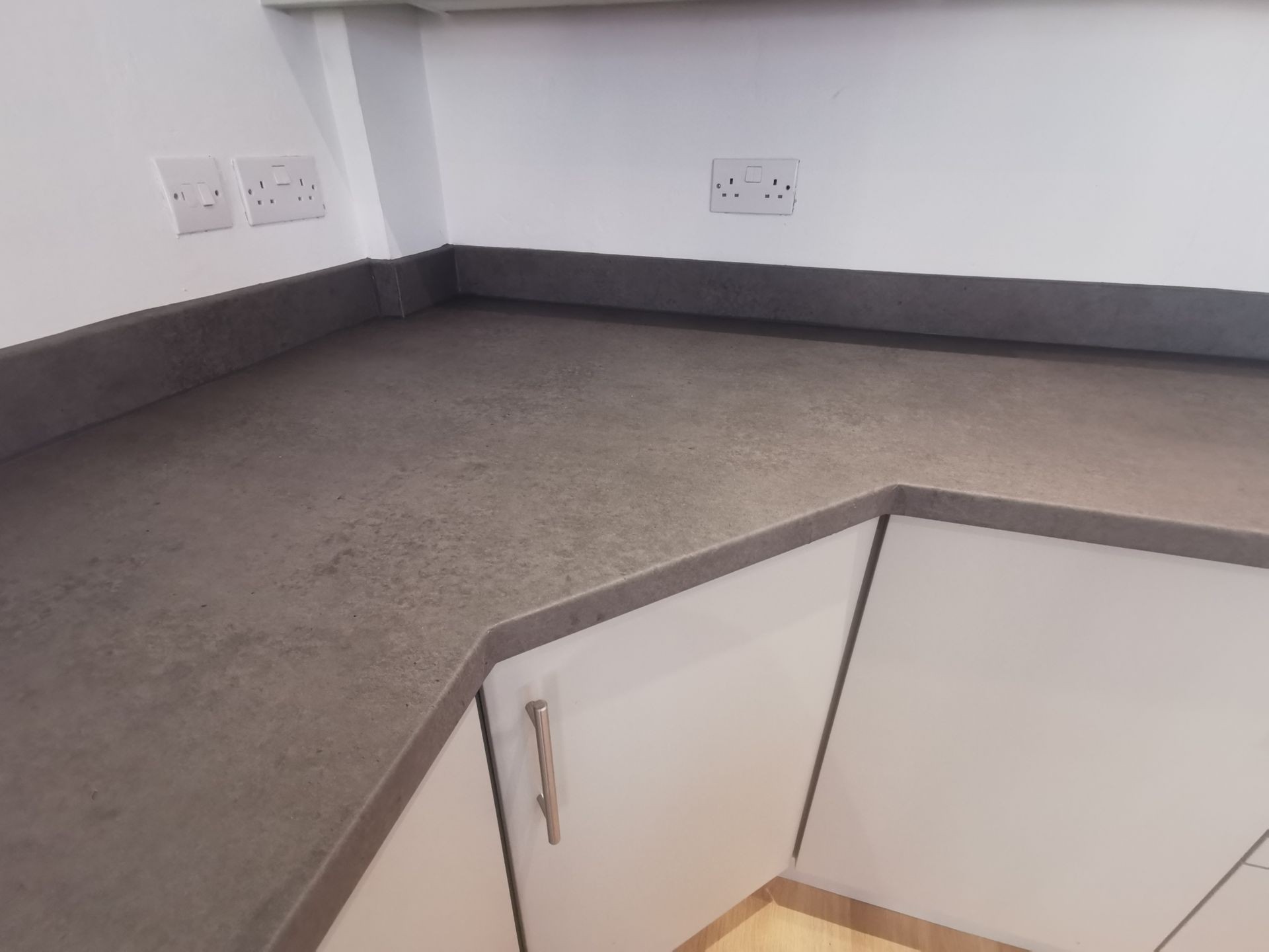 Kitchen countertop with dark surface, white cabinets, and wall sockets.